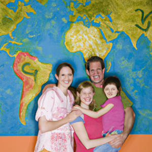 A happy family standing in front of a world map with their arms around each other.