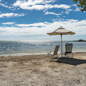 A sunlit beach with a sun chair and umbrella in the foreground and a peaceful ocean in the background.